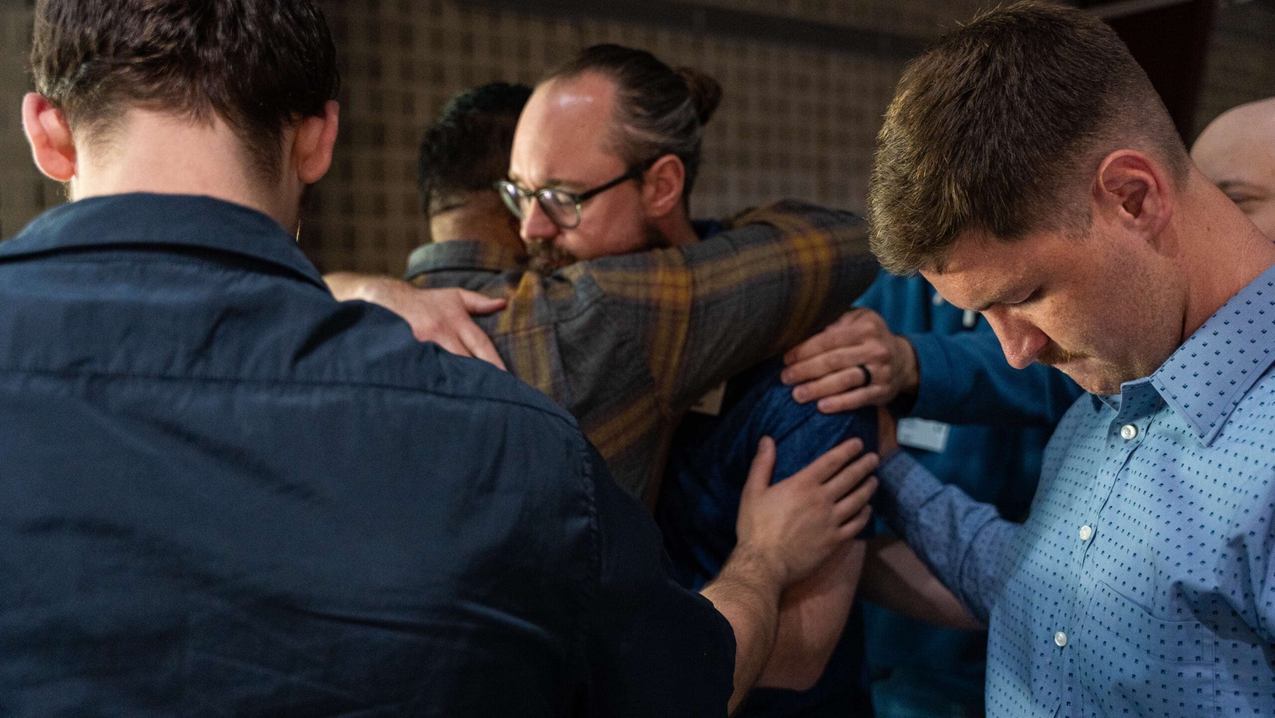 men gathered around praying and hugging